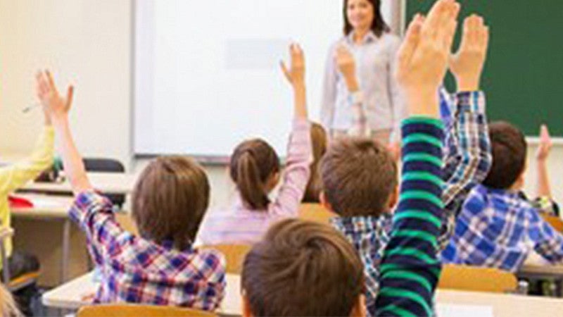 children sitting in a classroom with raised hands