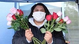 image of student in a face mask holding a bunch of pink colored roses in each hand