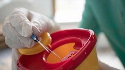 hands in white gloves putting a needle in syringe disposal