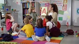 teacher kneeling talking to students sitting on the floor