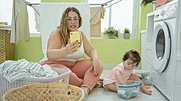 a person and baby sitting on laundry room floor holding a cell phone